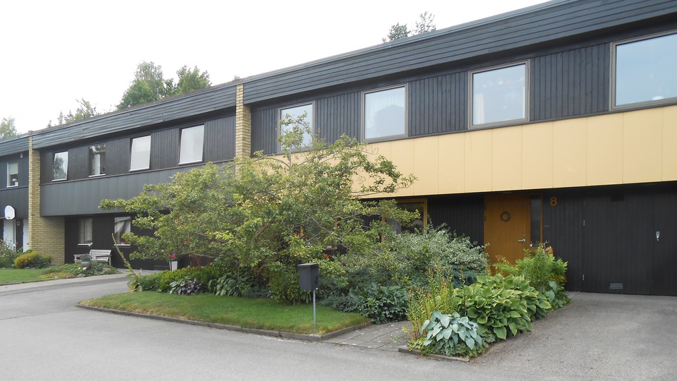 Svart hus med buskar framför