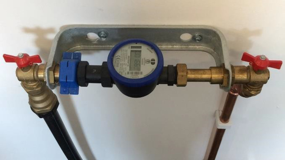 Exempel på en godkänd mätplats med konsol och snabbstängande ventiler fastmonterad lättillgänglig på en vägg. En plombering (blå plastklämma) är installerad till vänster om mätaren.